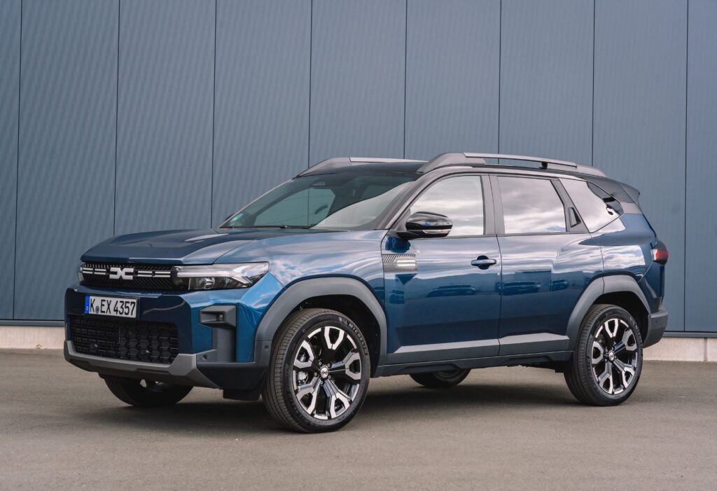 Blauer Dacia Bigster vor grauer Wand