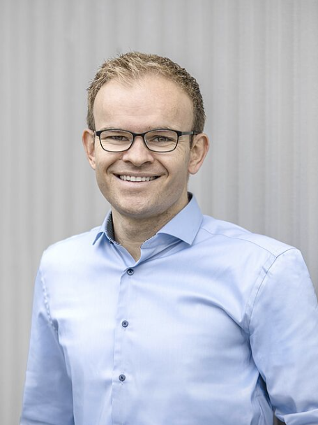 Mann in hellblauem Hemd steht.