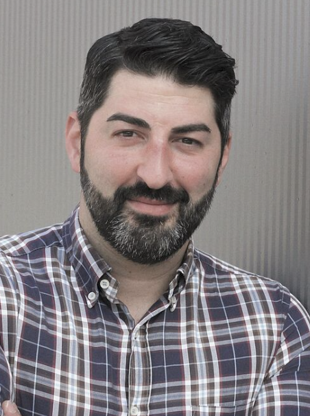 Mann mit kariertem Hemd, verschränkten Armen.