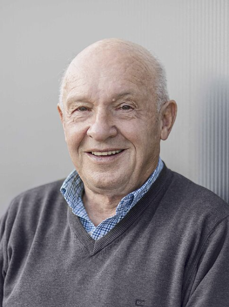 Älterer Mann in grauem Pullover.