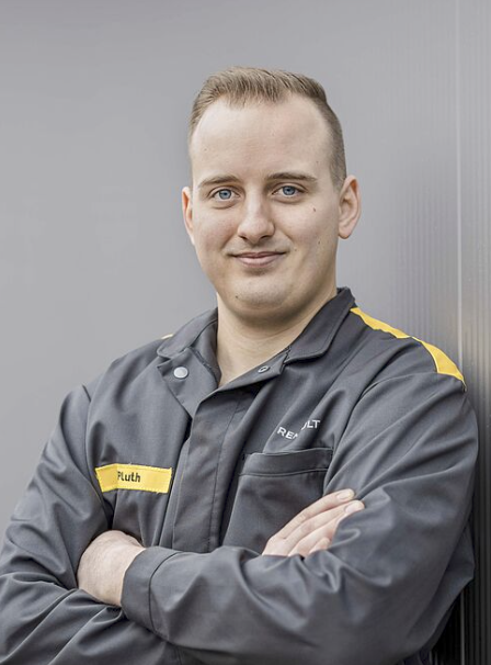 Mann in Arbeitskleidung mit Arm verschränkt.