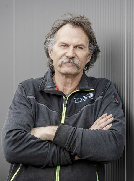 Mann mit verschränkten Armen steht.